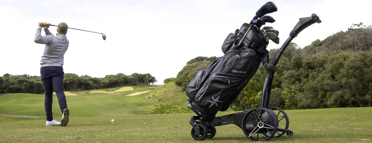 Electric remote golf buggy with golf bag on course, golfer swinging in background